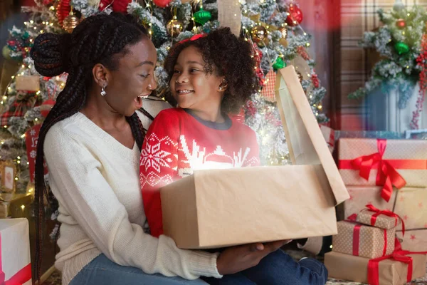 Mãe e filha africana feliz abrindo caixa de presente de Natal mágico — Fotografia de Stock