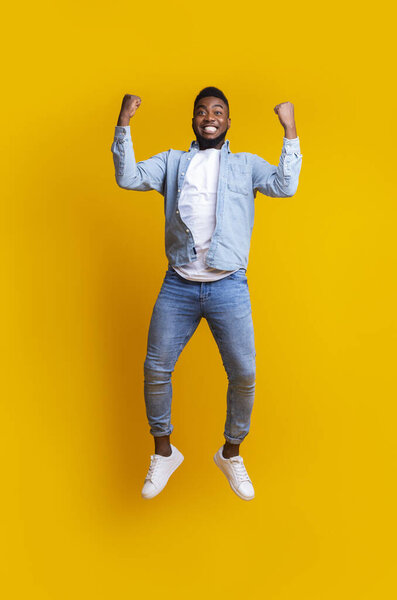 Эйфорический афро-парень, прыгающий в воздух, празднующий успех на жёлтом фоне
