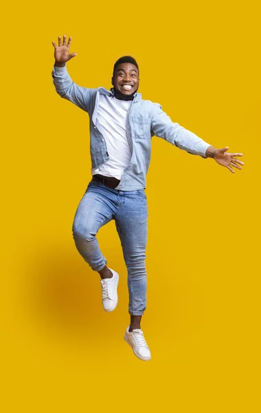 Веселый черный парень веселится, прыгая в воздухе на желтом фоне — стоковое фото