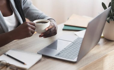 Ofiste dizüstü bilgisayarla çalışırken kahve içen Afro iş kadını.