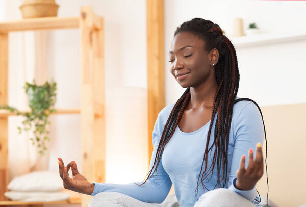 Афроамериканка медитирует в постели дома
