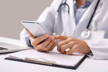 İş yerinde akıllı telefon kullanan erkek doktor, online danışmanlık yapıyor.