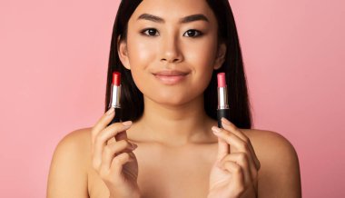Asyalı kız iki ruj rengi arasında seçim yapıyor.
