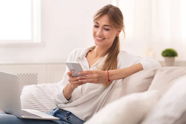 Woman Using Mobile Phone And Laptop Sitting On Couch Indoor — 图库照片