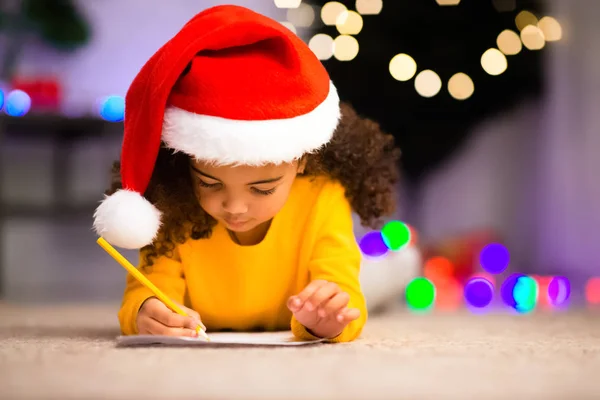 Menina preta bonito em Santa chapéu escrita apresenta lista para os pais — Fotografia de Stock