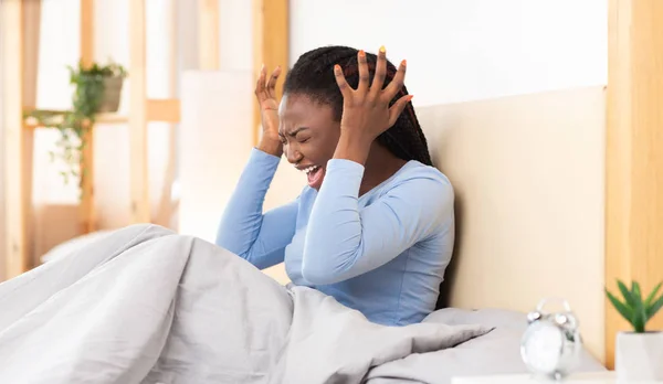 Emotionale schwarze Frau schreit, die Ohren bedeckt, im Schlafzimmer sitzend — Stockfoto