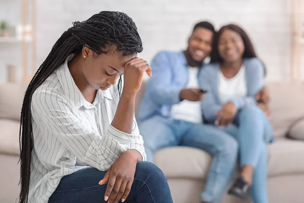 Menina ciumenta sentado sozinho enquanto ela namoro amigos abraçando no sofá — Fotografia de Stock