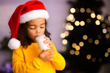 Küçük Afrikalı kız Noel ağacının yanında ılık süt içiyor.