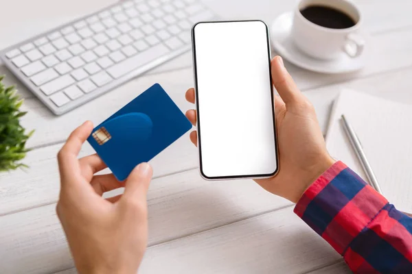 Homem segurando smartphone e cartão de crédito em branco, fazendo transação financeira — Fotografia de Stock