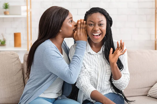 Duas jovens africanas americanas fofocando no sofá em casa — Fotografia de Stock