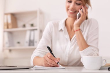 Girl Talking On Mobile Phone Taking Notes At Workplace, Cropped