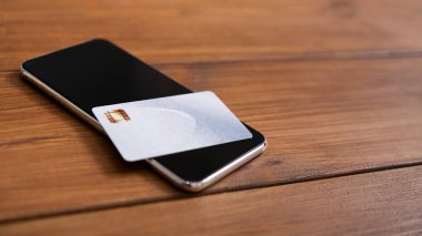 Siyah ekranlı akıllı telefon ve ahşap masada kredi kartı.