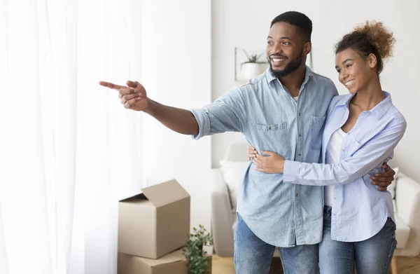 Afro manžel ukazuje manželka okno pohled objímání ve vlastním bytě — Stock fotografie