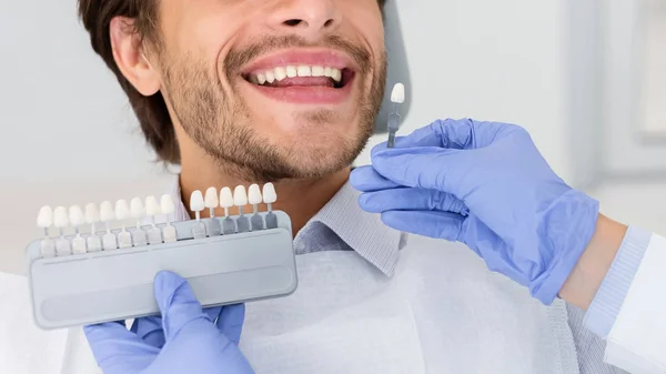 Dentysta nakładający próbkę ze skali zębów na uśmiechnięte zęby człowieka — Zdjęcie stockowe