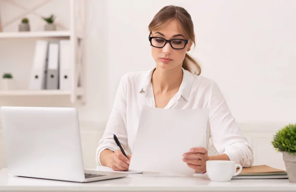 Büromädchen liest Geschäftsbericht und macht sich am Arbeitsplatz Notizen — Stockfoto