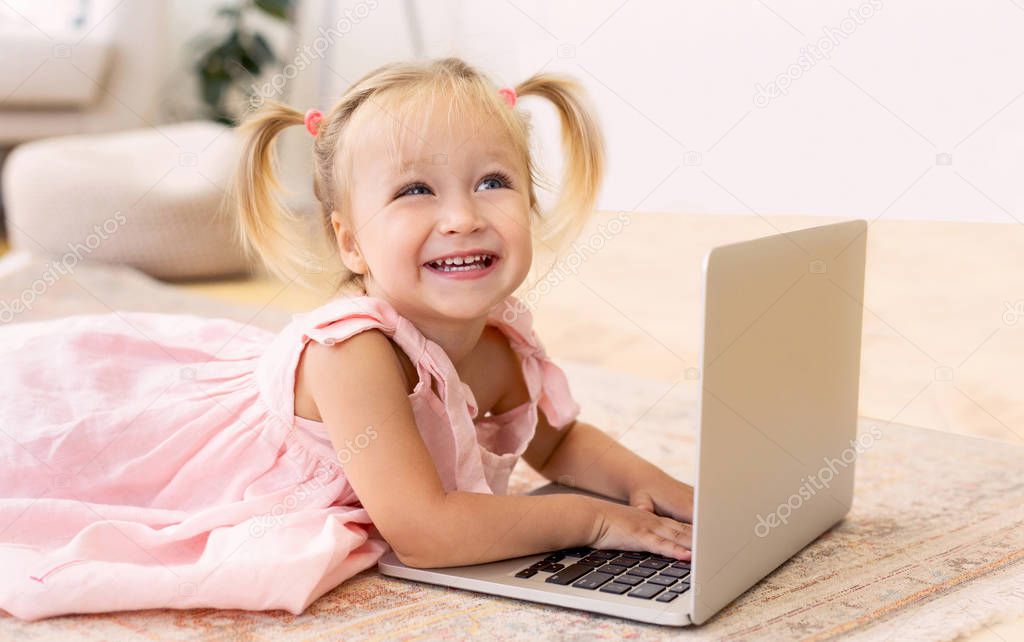 Adorable little girl using laptop lying on couch