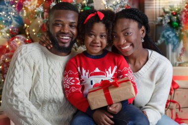 Üç kişilik neşeli siyah aile Noel ağacının yanında hediyelerle poz veriyor.