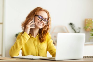 İş kadını telefonda konuşuyor ve ofiste dizüstü bilgisayarla çalışıyor.
