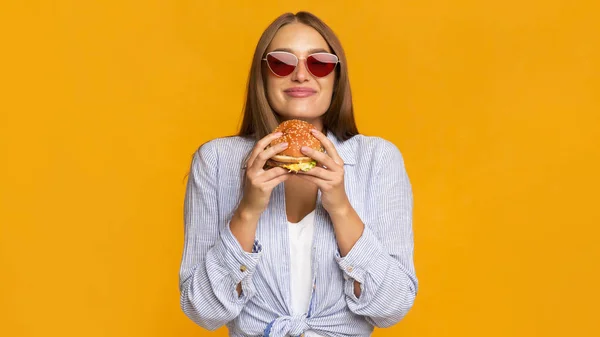 Stylish Millennial Girl Smelling Burger Standing In Studio, Panorama — стокове фото
