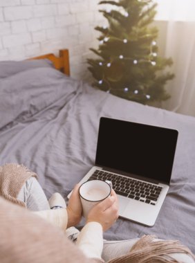 Woman with mug looking at open laptop with blank screen