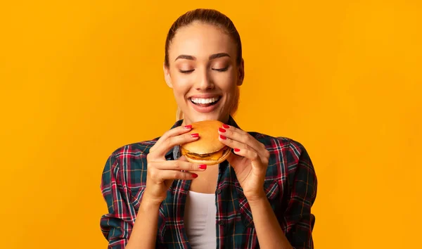 Glad ung kvinna äter hamburgare stående i studio — Stockfoto