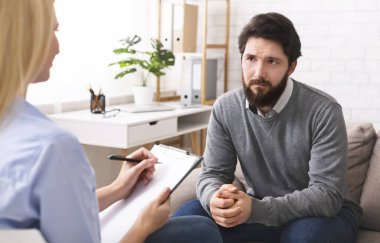 Stresli genç adam terapide psikologla konuşuyor.