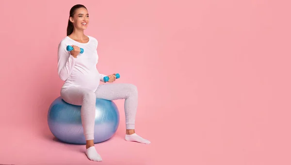 Zwanger meisje oefening met duimbellen zitten op Fitball, Roze achtergrond — Stockfoto