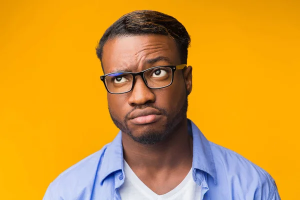 Hombre afroamericano desconcertado pensando en algo de pie, fondo naranja — Foto de Stock