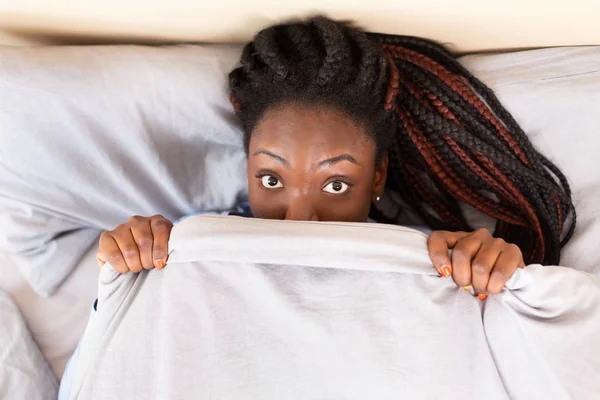 Afro chica espiando fuera de manta acostado en cama, Top-View —  Fotos de Stock