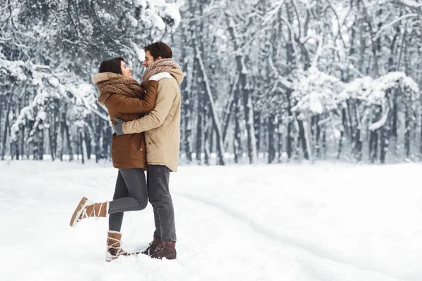 Пара обнимающихся, стоящих в снежном зимнем лесу утром — стоковое фото