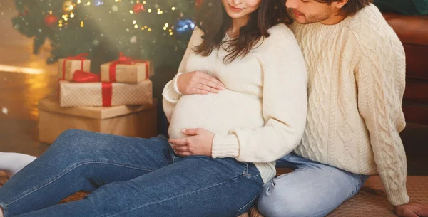 Koca kollu hamile kadın Noel ağacının yanında oturuyor. — Stok fotoğraf