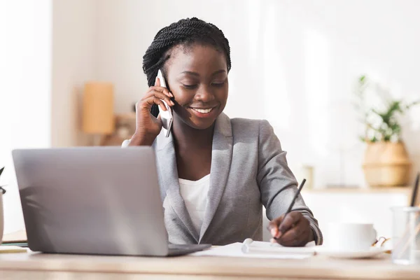 Afro Sekreter ofisinde not alıyor ve telefonla konuşuyor. — Stok fotoğraf