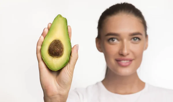 Mujer mostrando aguacate medio a cámara sobre fondo blanco —  Fotos de Stock