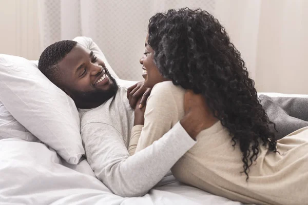 Lächelndes schwarzes Paar hat Spaß im Bett, umarmt und flirtet — Stockfoto