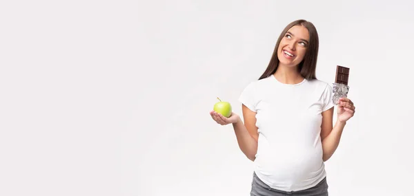 妊娠中の女性は灰色の背景にアップルとチョコレートを保持,パノラマ — ストック写真