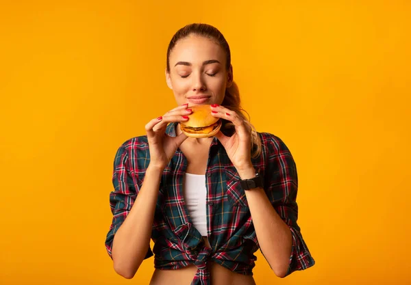 Menina Smelling Burger em pé sobre fundo de estúdio amarelo — Fotografia de Stock