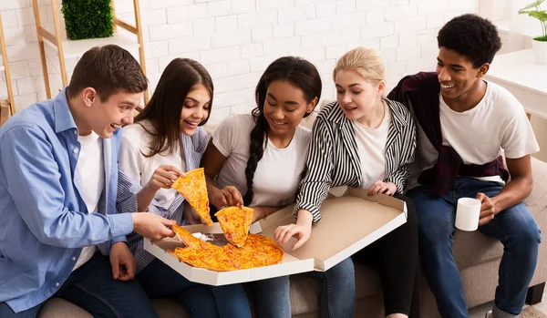 Colocataires adolescents mangeant une pizza chaude, prenant des tranches de la boîte de livraison — Photo