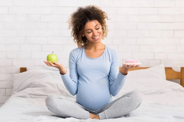 Gravidez e escolha de alimentos. Mulher expectante com maçã e donut — Fotografia de Stock