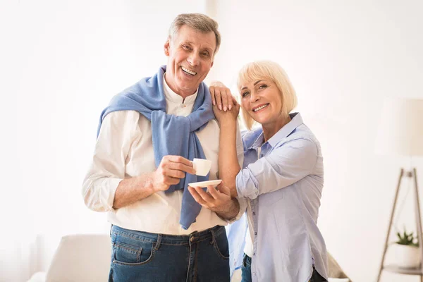 Щаслива старша пара посміхається до камери, чоловік п'є каву — стокове фото