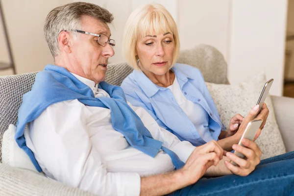 Modern grandparents. Senior couple using cellphones at home