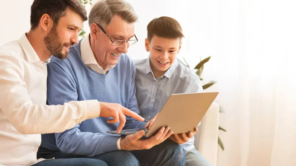 Старший использует ноутбук сидя с внуком и сыном в помещении — стоковое фото