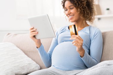 Bebek için kıyafet sipariş eden, tablet kullanan hamile bir kadın.