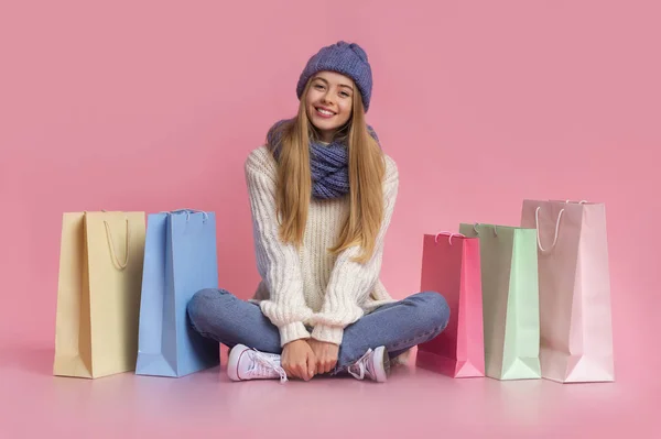 Zorgeloos blond meisje in de winter kleding zitten tussen winkeltassen — Stockfoto