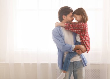 Genç baba küçük anaokulu kızını kucağında tutuyor.