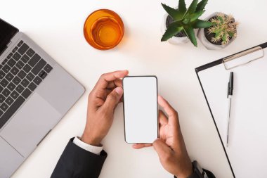 Takım elbiseli adam çalışma masasında boş akıllı telefon kullanıyor.