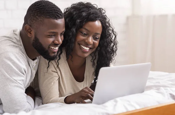 Glückliches afroamerikanisches Paar benutzt Laptop, während es zusammen im Bett liegt — Stockfoto