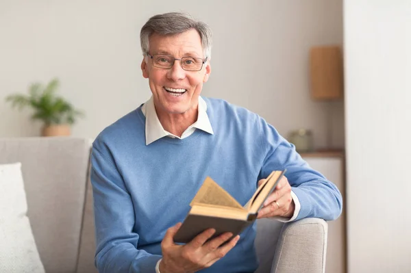 Senior Man holding Book Mosolygós Ül a kanapén beltéri — Stock Fotó
