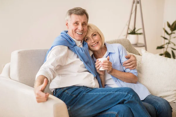 Feliz pareja de ancianos relajándose en el sofá y disfrutando del té de la mañana —  Fotos de Stock