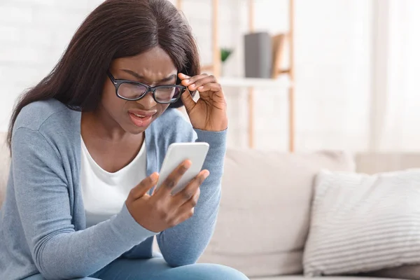 Impresionado negro chica en gafas mirando a la pantalla del teléfono celular con incredulidad —  Fotos de Stock