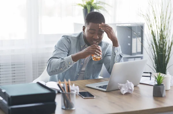 Hombre de negocios negro cansado bebiendo alcohol en el lugar de trabajo —  Fotos de Stock